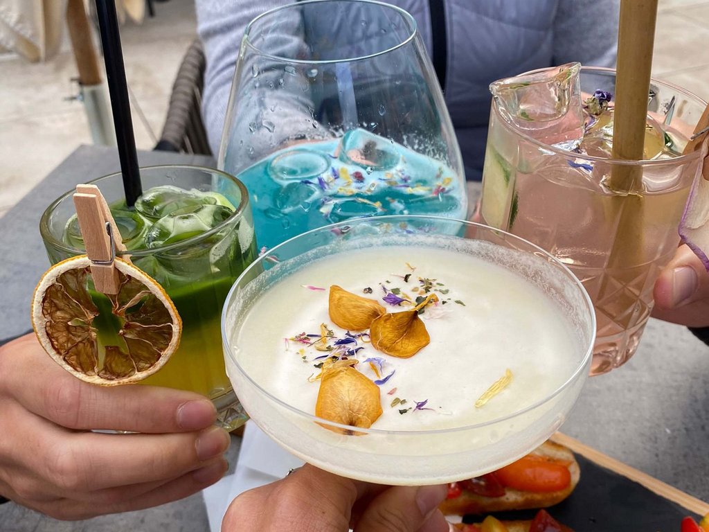 Fassatal: Wetter für Cocktailfans Vier Personen stoßen mit bunten Cocktails und Vorspeisen am Außentisch an