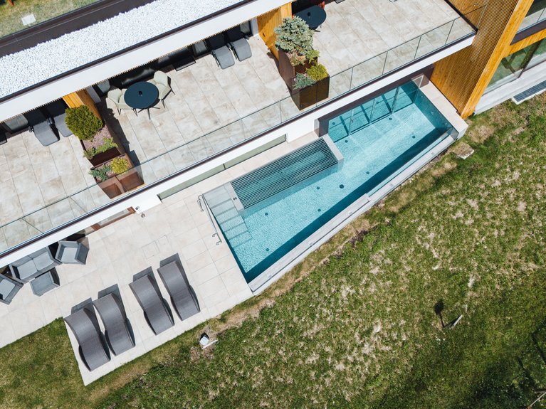 Hotel Latemar mit Dolomitenblick Moderne Terrasse mit Liegestühlen und Pool neben Holzbau.