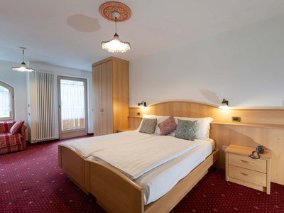 Hotel a Soraga in Val di Fassa: camere & suites Camera da letto con letto matrimoniale, armadio, divano rosso e moquette rossa