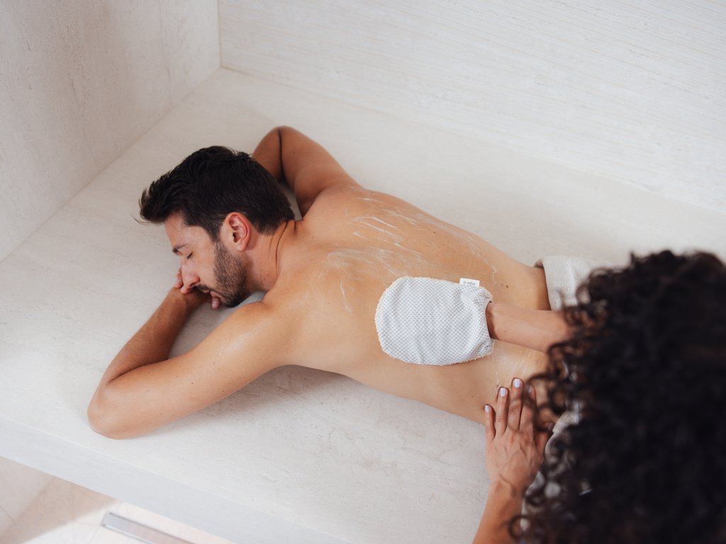 A Soraga il meteo è sempre ottimo per un Day Spa! Uomo sdraiato mentre riceve un massaggio alla schiena con guanto esfoliante