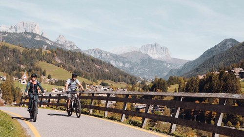 Paussa Suite Two people cycling on a mountain road with alpine landscape