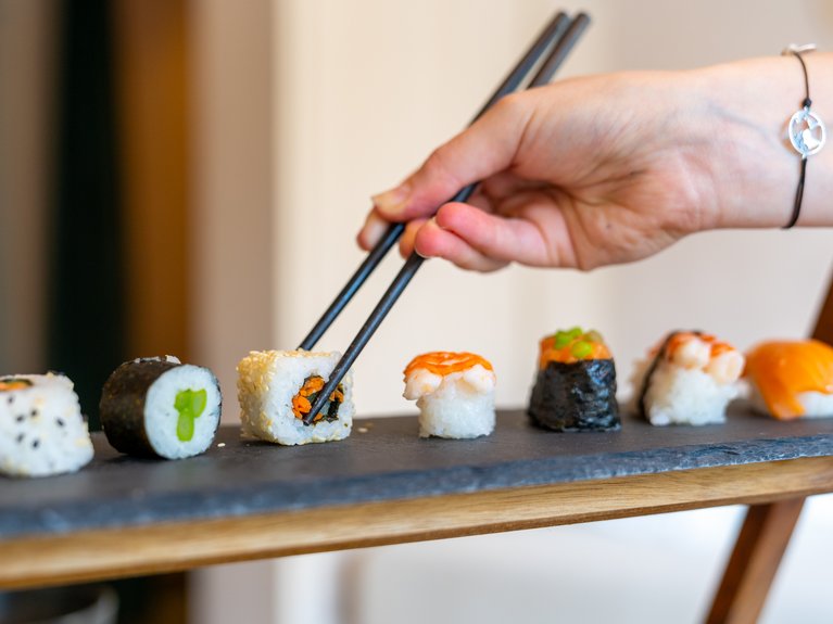 Urlaub im Fassatal: Erholung pur Hand nimmt Sushi mit Essstäbchen von einem Tablett