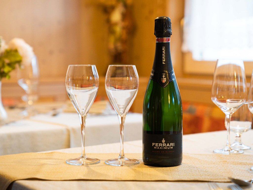 Per buongustai: l’hotel ideale vicino a Moena Bottiglia di Ferrari Maximum e due flute vuoti su tavolo apparecchiato