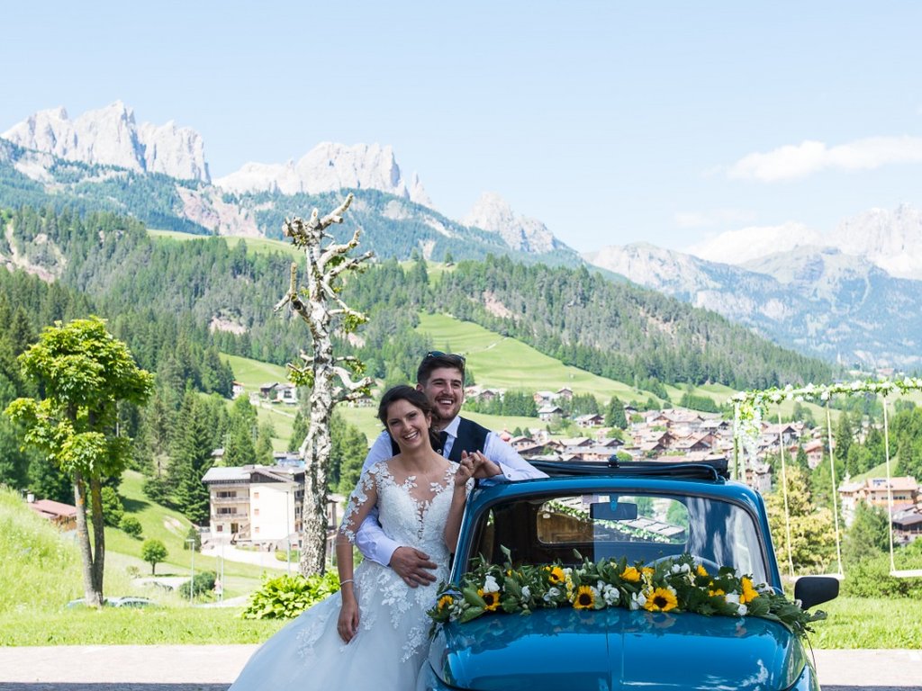 Val di Fassa: wandern, biken, erleben Brautpaar neben einem mit Blumen dekorierten Oldtimer-Fiat vor Berglandschaft