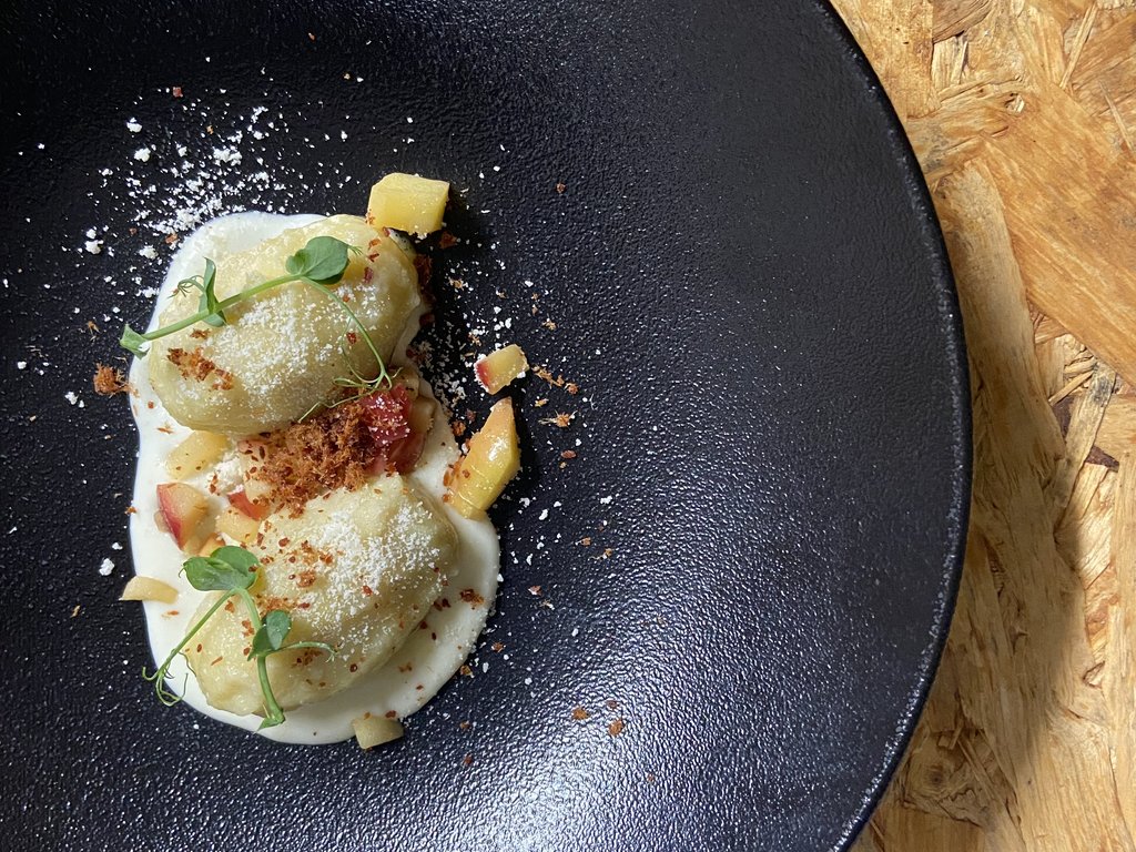 Per buongustai: l’hotel ideale vicino a Moena Due gnocchi con crema bianca, cubetti di frutta e decorazioni verdi su piatto nero