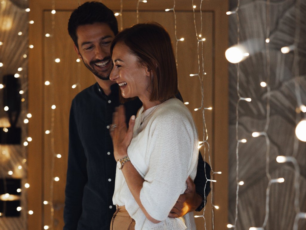 Sulla pista ciclabile, da Moena alla vostra oasi romantica Coppia sorridente abbracciata davanti a luci decorative in casa