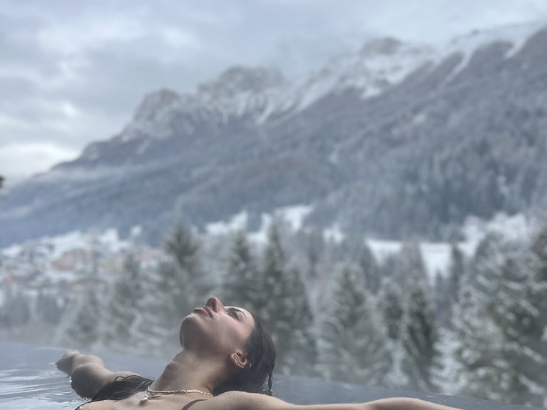 Urlaub im Fassatal: Erholung pur Frau entspannt im Infinity-Pool mit Blick auf verschneite Berge