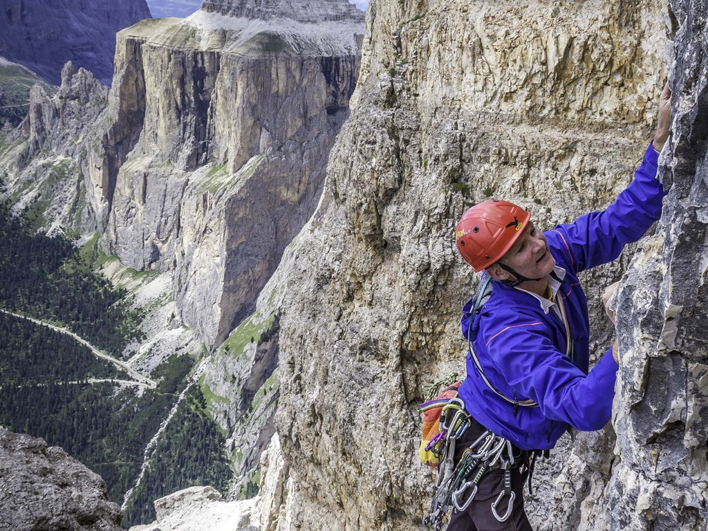 Lago di Soraga and summer activities near Hotel Latemar Climber with red helmet ascending a rock face in the Dolomite mountains