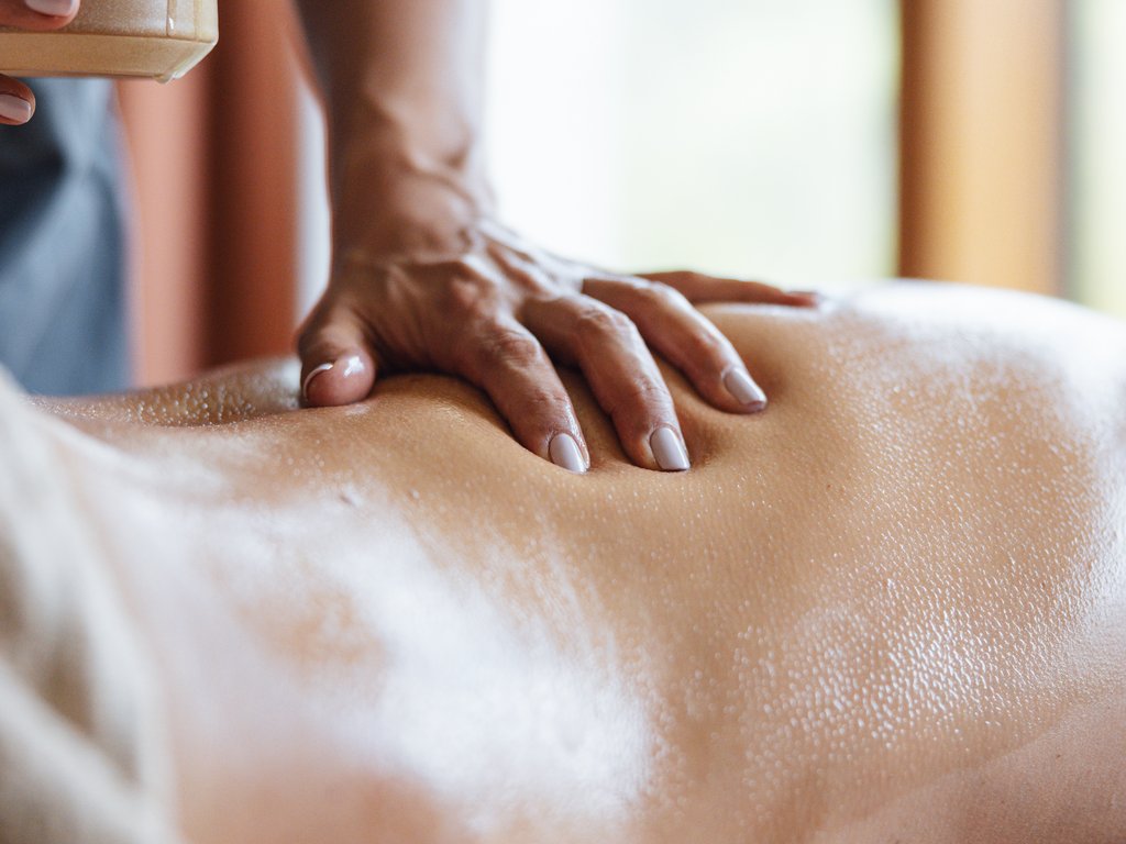 Trentino: Hotel am See mit Pool und Spa Hand massiert den geölten Rücken einer Person bei einer entspannenden Massage