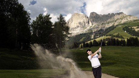 Picture gallery Golfer hitting ball from sand bunker with mountains in the background