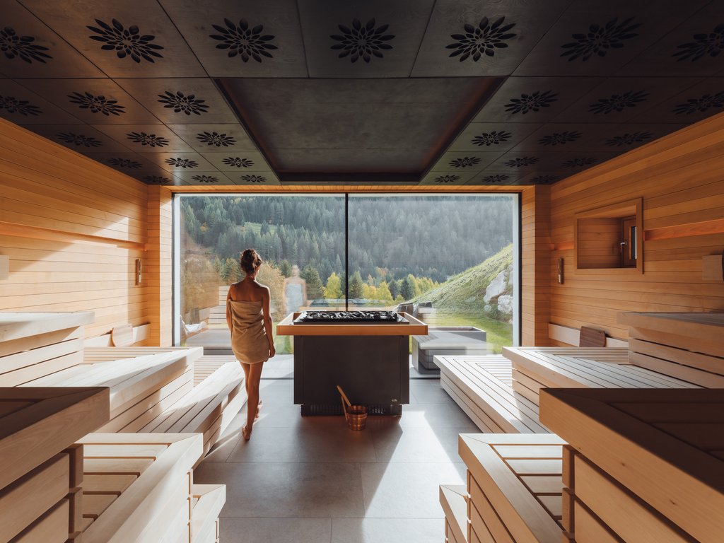 Al Latemar, dopo le passeggiate: relax nella Spa Oniro Donna in accappatoio in sauna con vista sulle montagne attraverso una finestra grande