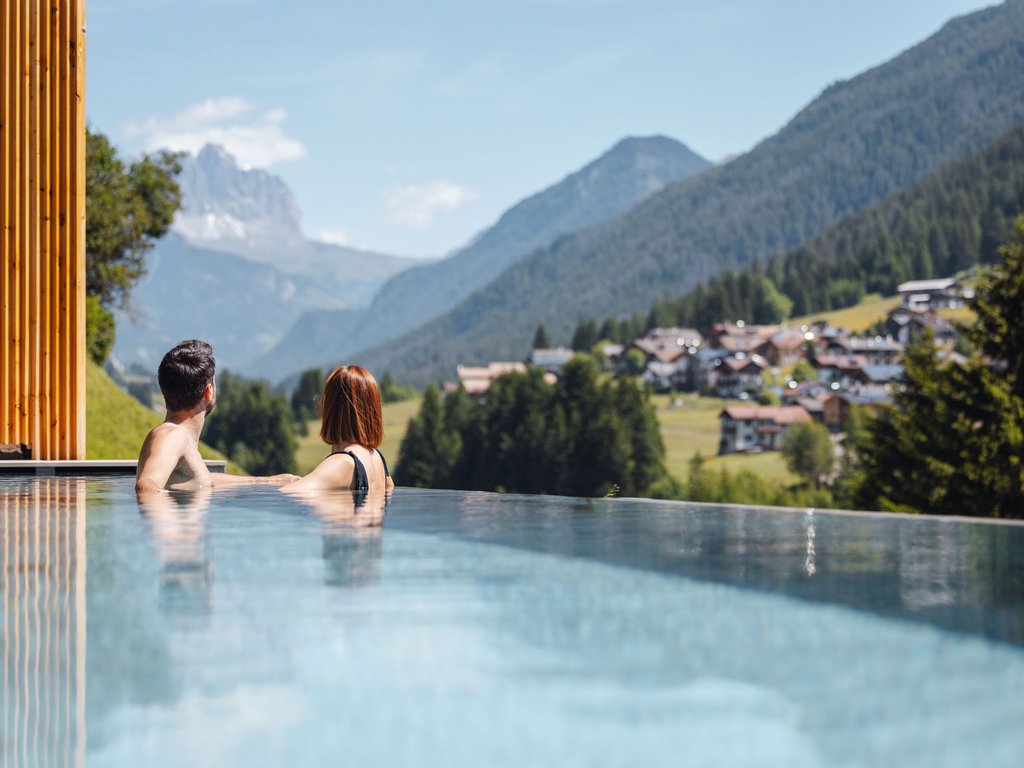 Hotel Latemar mit Dolomitenblick Paar im Infinity-Pool mit Blick auf Berge und ein Dorf