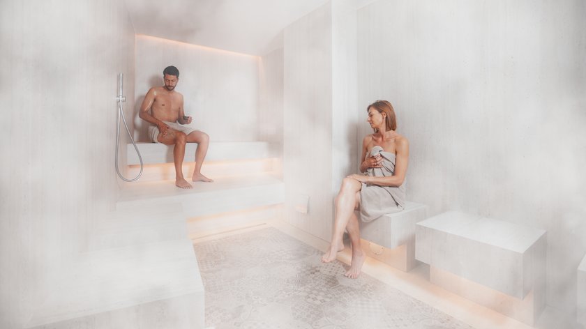 Trattamenti Latemar Signature: un mondo di benessere Due persone rilassate nella sauna moderna con pareti chiare e pavimento piastrellato