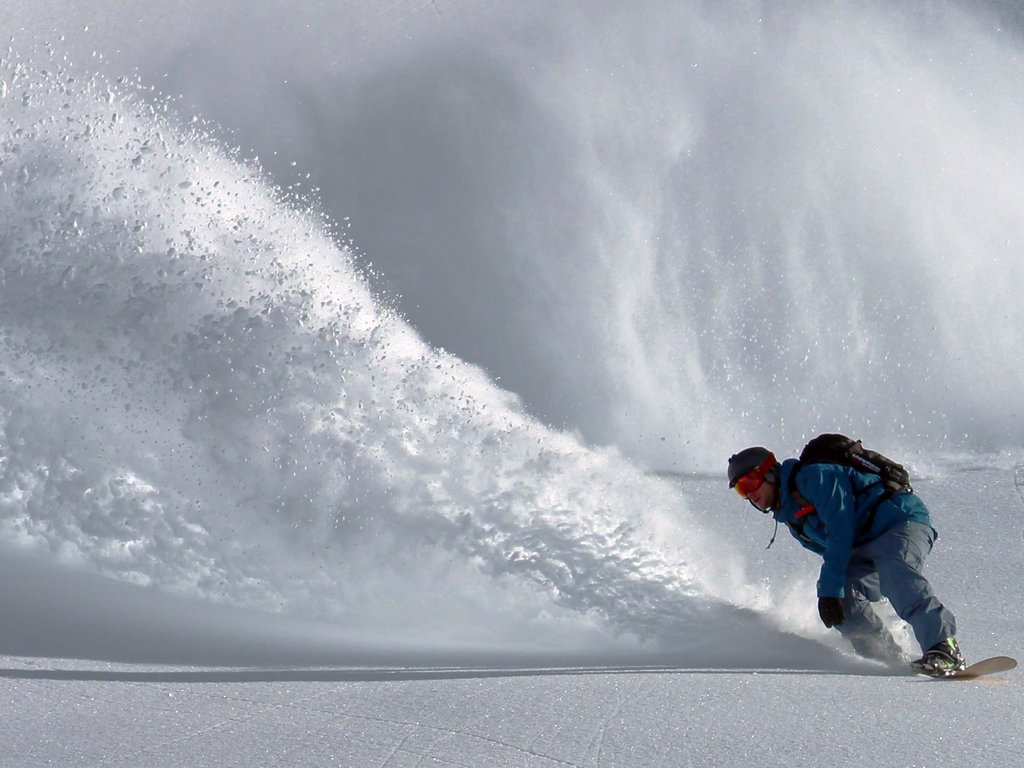 Passeggiate invernali in Val di Fassa: Hotel Latemar Snowboarder che scende su neve fresca con grande spruzzo di neve