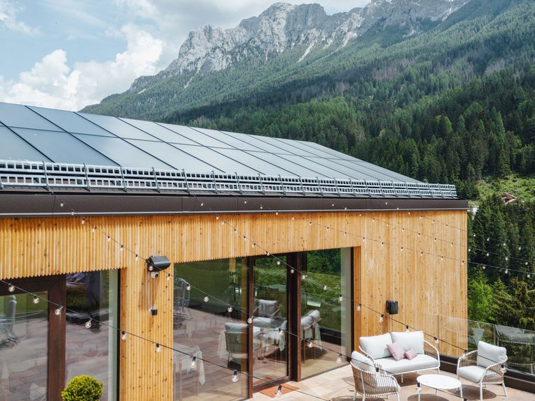 Hotel Latemar mit Dolomitenblick Terrasse mit modernen Sitzmöbeln und Lichterketten vor Holzgebäude mit Bergen im Hintergrund