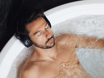 Barrierefreies Hotel im Val di Fassa: das Latemar Mann entspannt in Badewanne mit Kopfhörern und sprudelndem Wasser