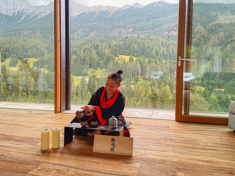 Hotel Latemar mit Dolomitenblick Frau bereitet japanische Teezeremonie in einem Raum mit Bergblick vor