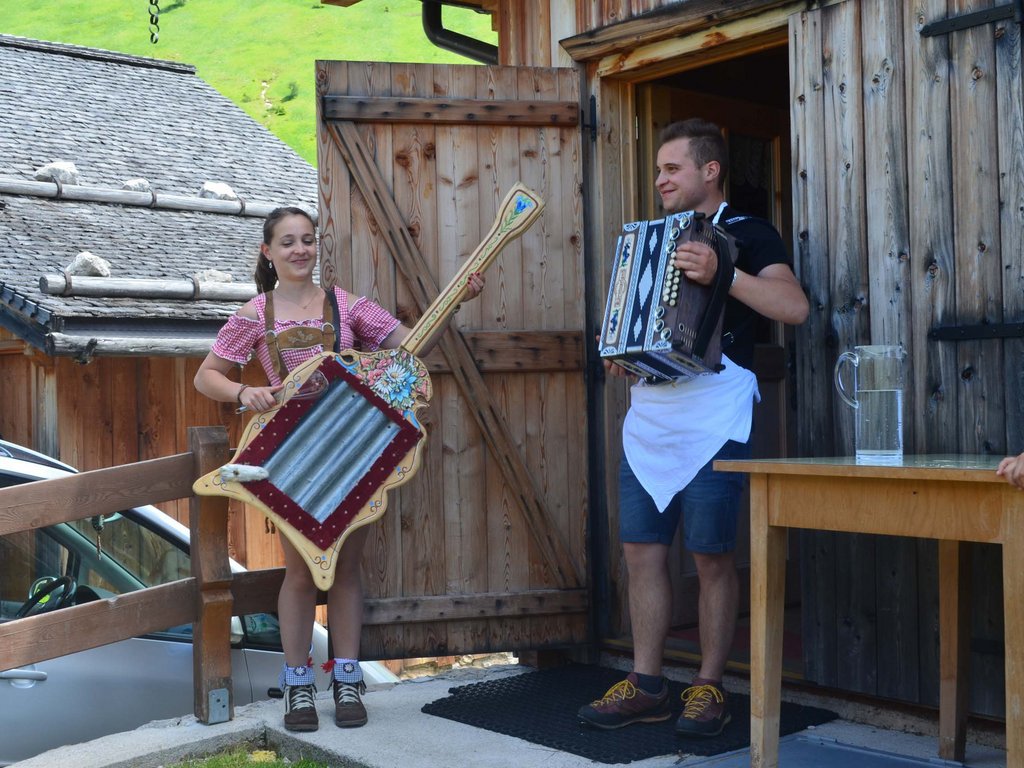 Per buongustai: l’hotel ideale vicino a Moena Due persone suonano strumenti musicali tradizionali davanti a una casa di legno