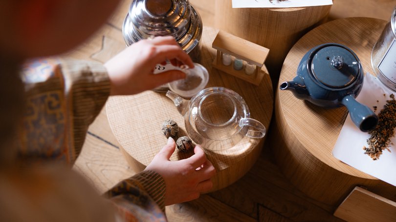 Val di Fassa: wandern, biken, erleben Person bereitet Tee mit Teekannen und Teeblättern auf Holzpodesten zu