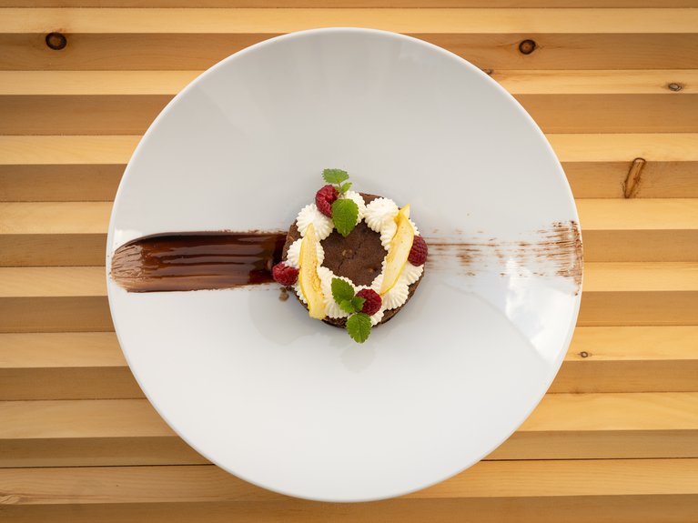 Restaurant Mirage mit Dolomiten-Blick im Fassatal Schokoladendessert mit Sahne, Himbeeren und Minzblättern auf weißem Teller