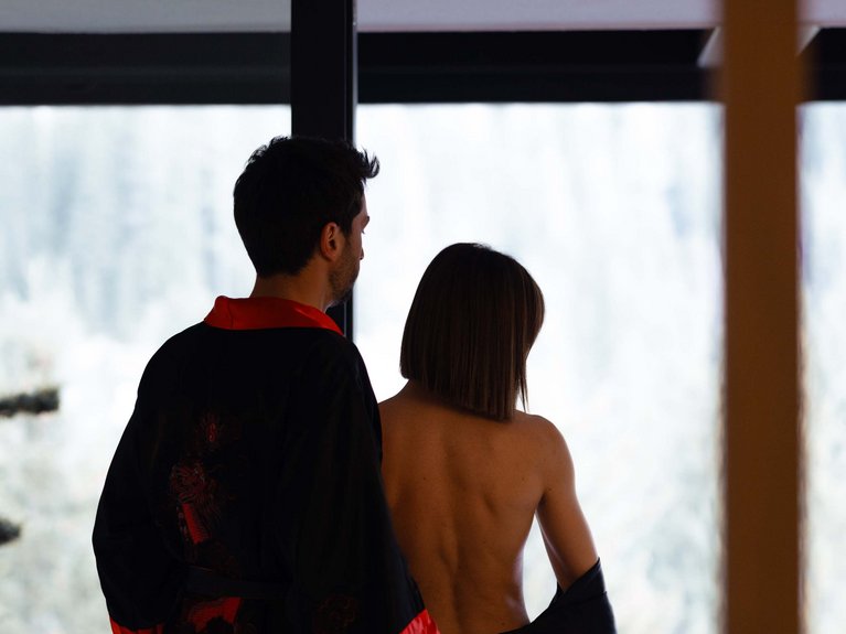 Urlaub im Fassatal: Erholung pur Paar in schwarzen und roten Bademänteln blickt aus dem Fenster