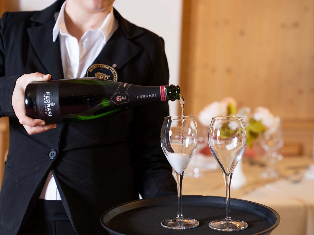 Passeggiate in Val di Fassa in inverno e pietanze deliziose Cameriere che versa vino spumante Ferrari in due bicchieri da flûte