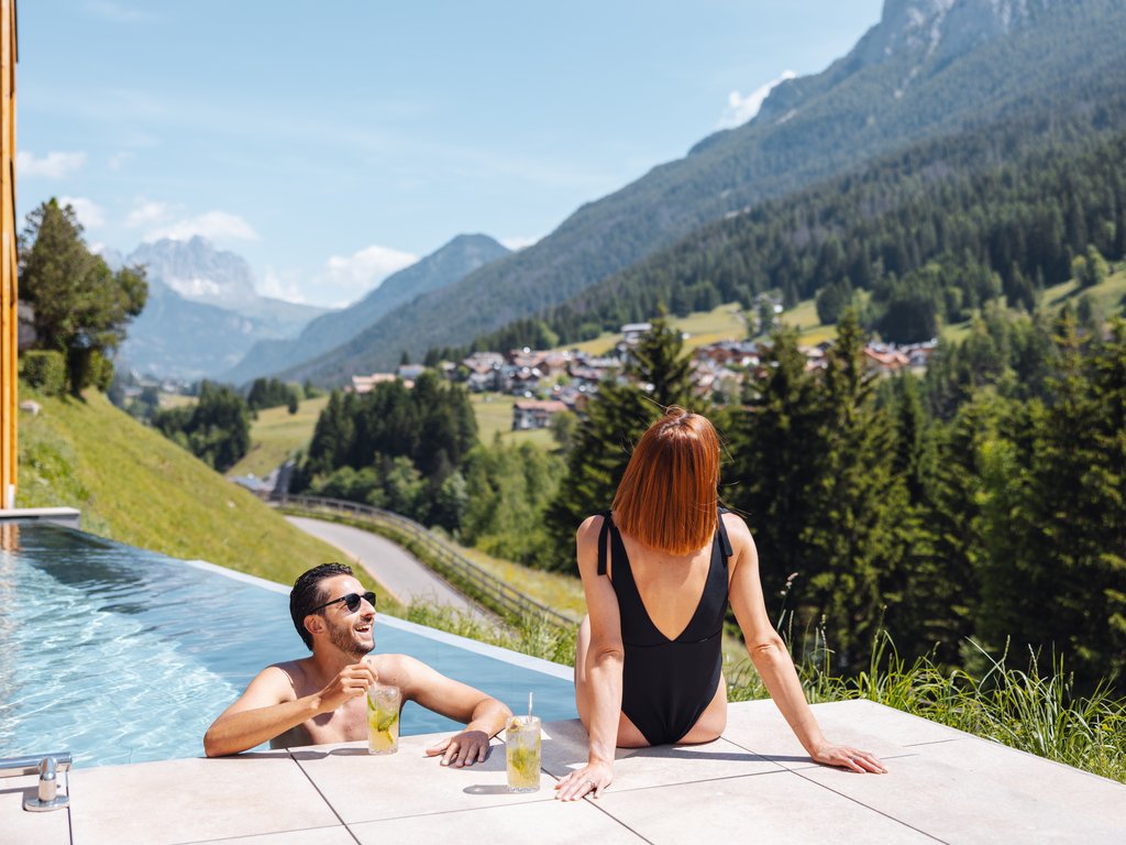 A Soraga il meteo è sempre ottimo per un Day Spa! Coppia che si rilassa in piscina con vista sulle montagne in una giornata di sole
