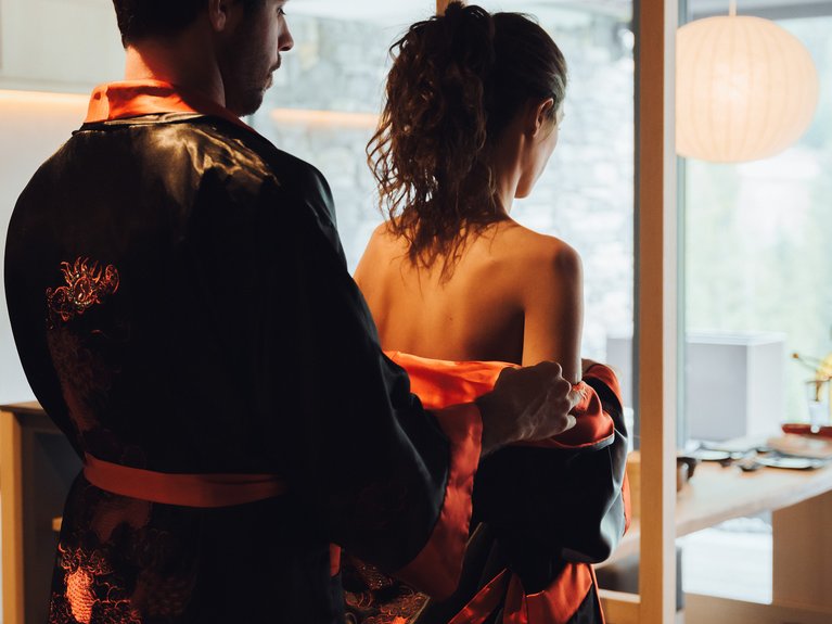 Sulla pista ciclabile, da Moena alla vostra oasi romantica Uomo che aiuta donna a indossare una vestaglia nera e rossa in una stanza moderna