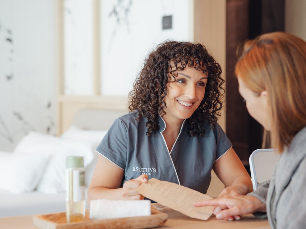 Trentino: Hotel am See mit Pool und Spa Kosmetikerin zeigt einer Kundin die Behandlungsliste im Spa