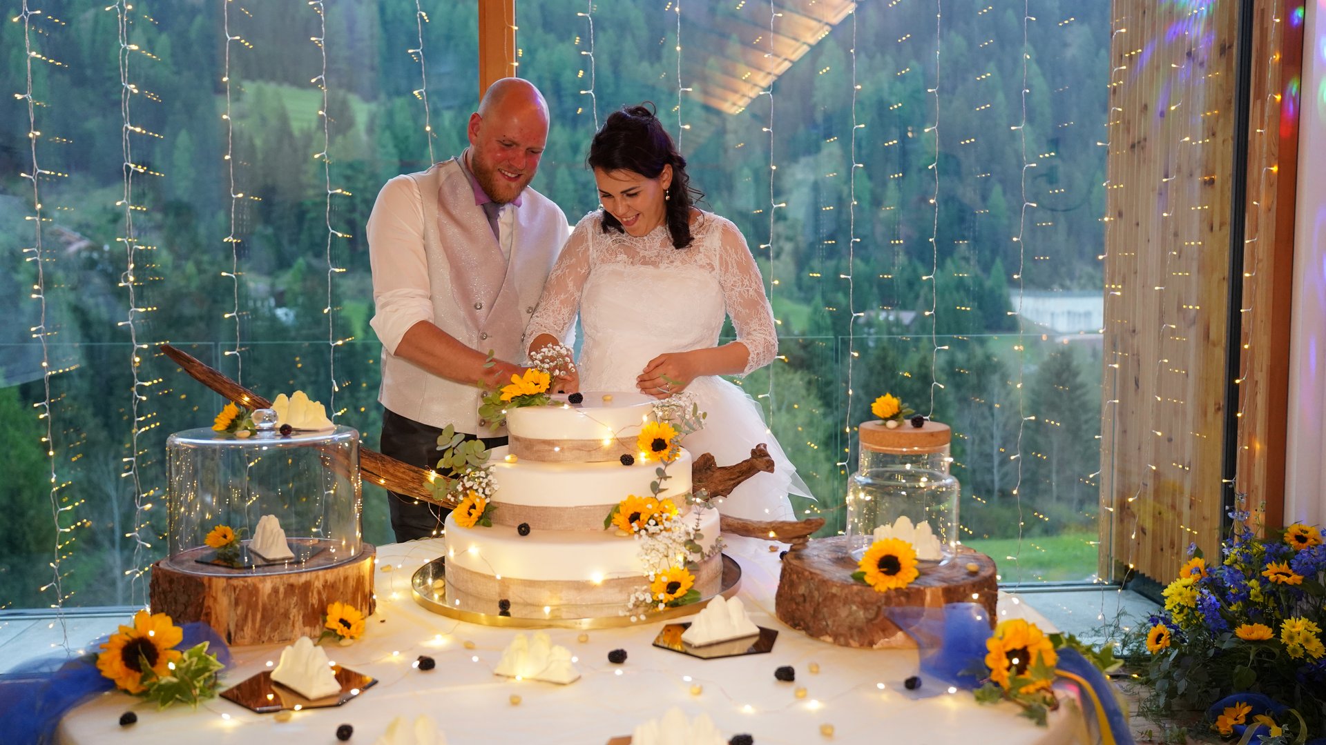Dalla webcam il Latemar è bello, ma dal vivo è un sogno! Sposi felici tagliano una torta nuziale con girasoli e luci decorative