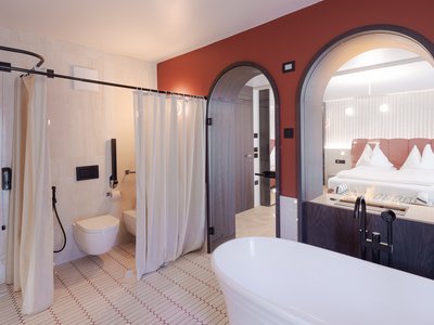 Barrierefreies Hotel im Val di Fassa: das Latemar Modernes Badezimmer mit weißer Badewanne, Duschvorhang und bogenförmigem Spiegel