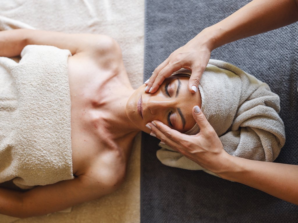 Trentino: Hotel am See mit Pool und Spa Frau bekommt Gesichtsbehandlung in Spa mit Handtuch um den Kopf