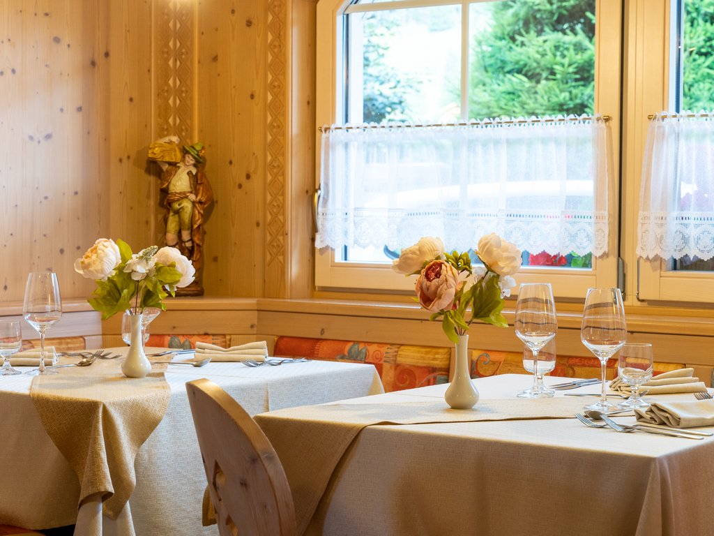Per buongustai: l’hotel ideale vicino a Moena Tavoli apparecchiati con fiori in un ristorante accogliente con pareti in legno