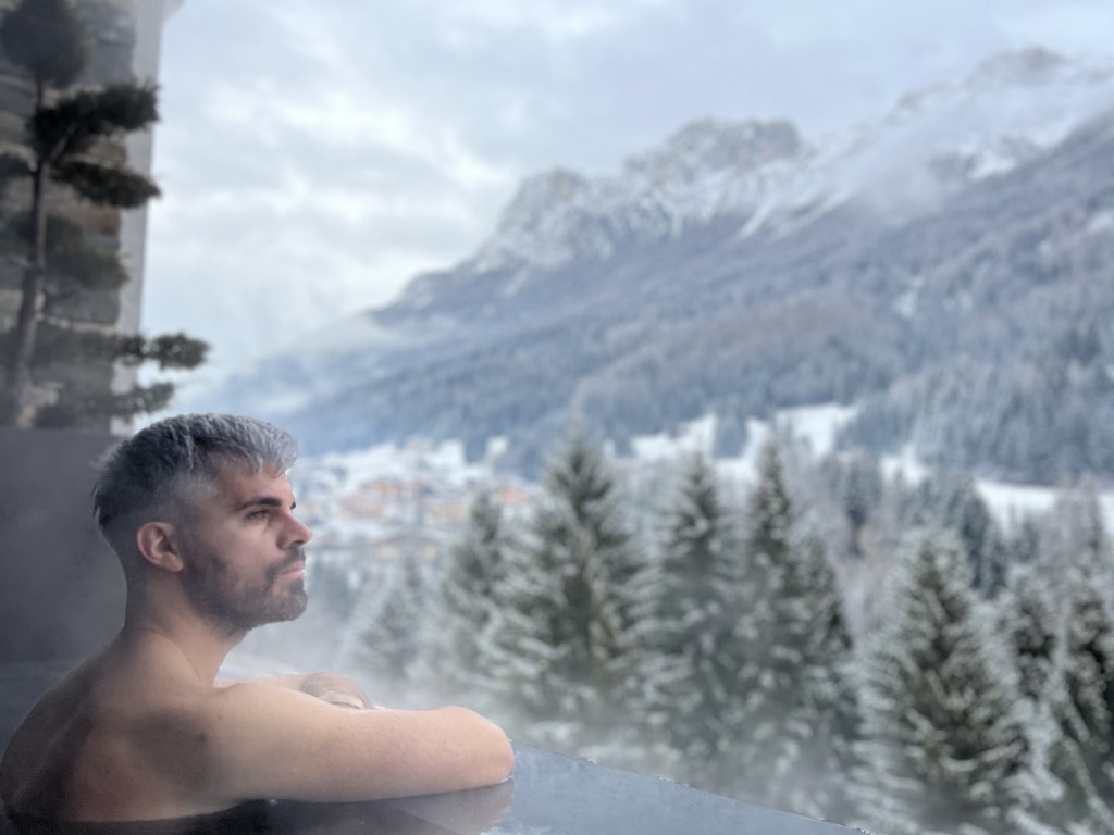 Urlaub im Fassatal: Erholung pur Mann entspannt in Whirlpool mit Blick auf verschneite Berge