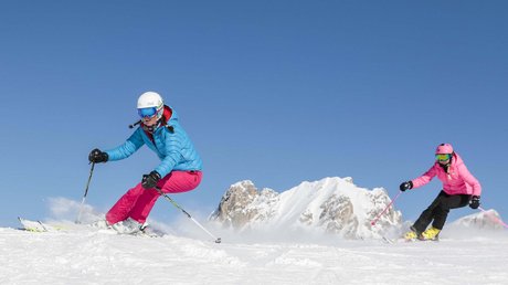 Meteo, Moena, Soraga, Latemar: tutto nella nostra gallery Due donne che sciano su neve fresca con montagne innevate e cielo blu