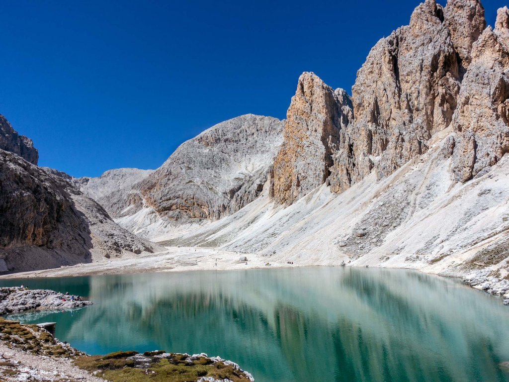 Lago di Soraga and summer activities near Hotel Latemar Calm alpine lake surrounded by rocky mountains under clear blue sky