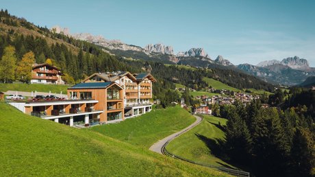 Picture gallery Wooden hotel on green hills with mountains and village in the background
