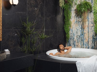 Barrierefreies Hotel im Val di Fassa: das Latemar Mann entspannt in Whirlpool mit Kopfhörern in modernem Badezimmer mit Pflanzen