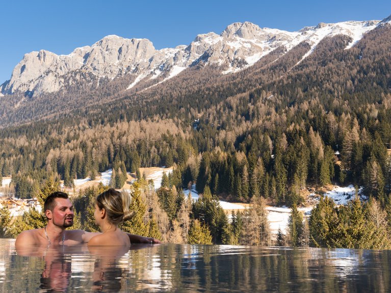 Urlaub im Fassatal: Erholung pur Paar im Pool mit Blick auf verschneite Berge und Wald