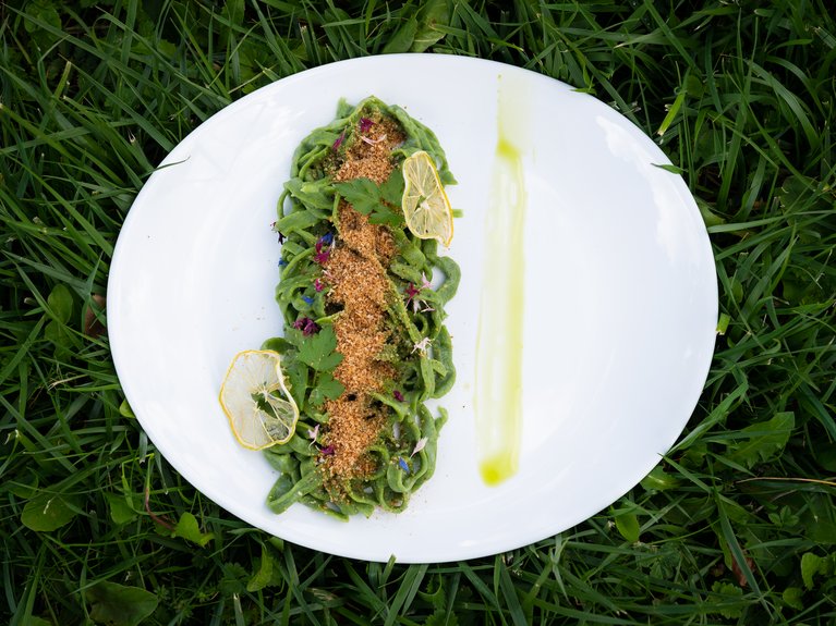 Hotel Latemar mit Dolomitenblick Teller mit grüner Pasta, Semmelbröseln und Zitronenscheiben auf grünem Gras