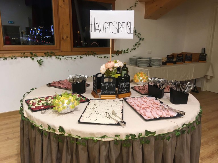 Dalla webcam il Latemar è bello, ma dal vivo è un sogno! Buffet con affettati, piatti principali e posate su tavolo rotondo decorato.