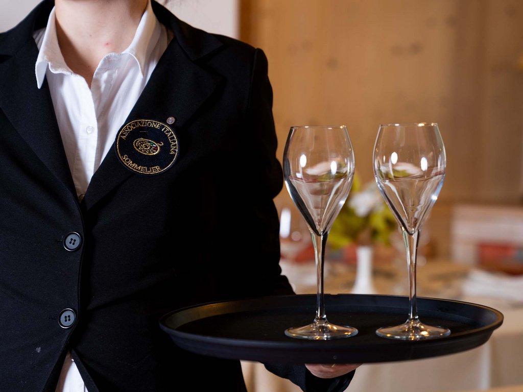 Per buongustai: l’hotel ideale vicino a Moena Sommelier con due bicchieri di vino su un vassoio nero