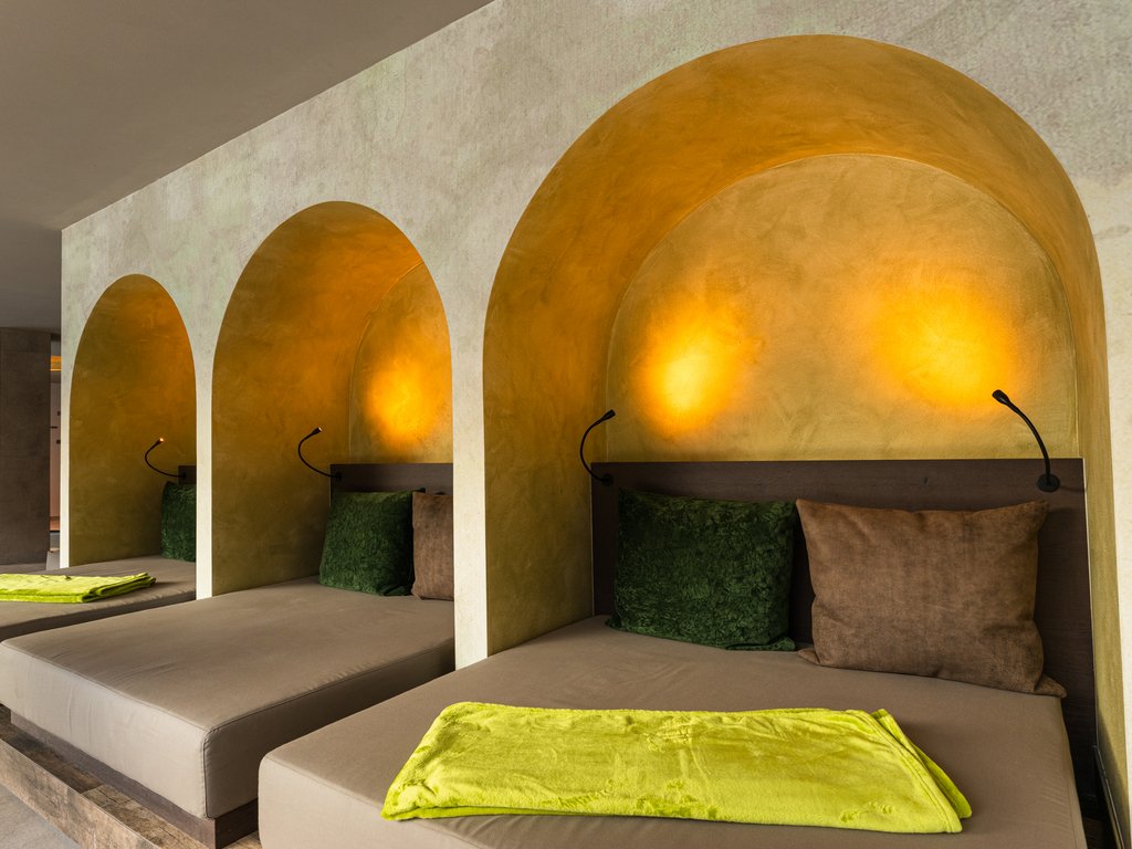 Soraga: dal lago alla piscina del Latemar Lettini con nicchie illuminate, cuscini verdi e marroni e coperte giallo lime.