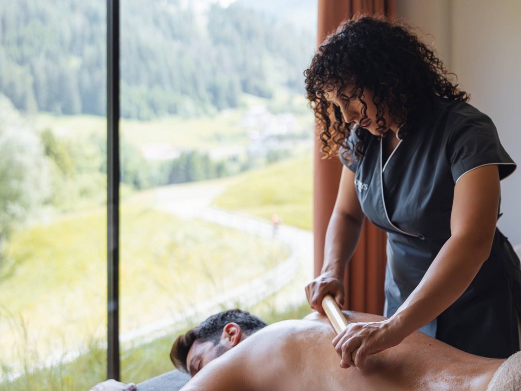 Latemar Signature treatments: a world of well-being Masseuse giving a back massage to a man near a window with a mountain view