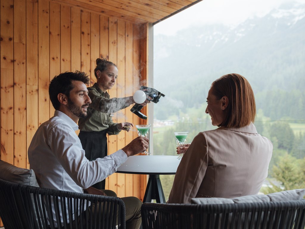 Sulla pista ciclabile, da Moena alla vostra oasi romantica Coppia che riceve cocktail fumanti serviti da barista su terrazza di montagna