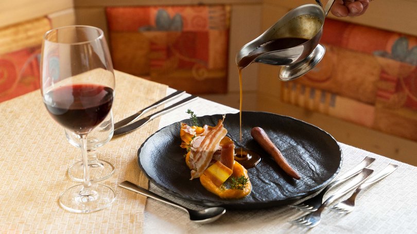 Moena, alberghi da sogno, panorama? C’è l’Hotel Latemar! Piatto gourmet con salsa versata e bicchiere di vino rosso a tavola