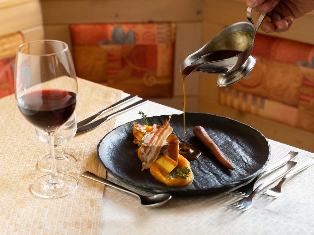 Mirage restaurant with a view of the Val di Fassa Dolomites Gourmet dish with sauce being poured and glass of red wine on table