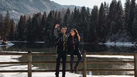Meteo, Moena, Soraga, Latemar: tutto nella nostra gallery Coppia in abbigliamento da trekking fa un selfie su una barriera con lago e alberi innevati