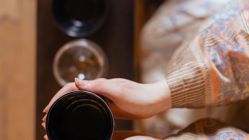 Val di Fassa: wandern, biken, erleben Hände halten eine schwarze Tasse über einem Tisch mit Gläsern