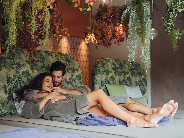 Sulla pista ciclabile, da Moena alla vostra oasi romantica Coppia rilassata abbracciata in accappatoi in ambiente con piante sospese